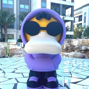 May include: A 3D-printed figure of a duck wearing a purple hoodie and black sunglasses. The duck has a yellow head, a white beak, and black pants with purple accents on the shoes. The figure is standing on a mosaic tile surface.