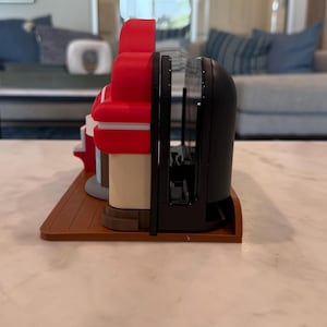 May include: A set of decorative bookends featuring a diner design. The bookends are red, white, and black, with a brown base. The bookends are made of plastic and are designed to hold books upright.