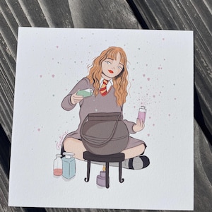Peut inclure: Illustration d'une personne en uniforme scolaire gris, mélangeant des potions dans un chaudron. La personne a les cheveux roux et est assise sur un petit tabouret. Des flacons de potion et une bougie allumée sont à proximité. L'œuvre est sur fond blanc.
