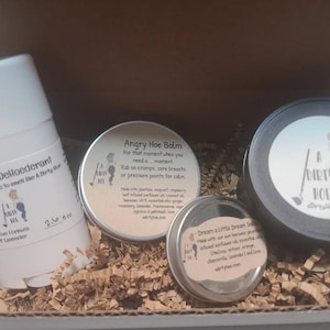 May include: A gift box filled with three small round containers. The containers are labeled "Angry Hoe Balm", "Dream a Little Dream Soap", and "A Dirty Hoe". The containers are surrounded by brown packing peanuts.