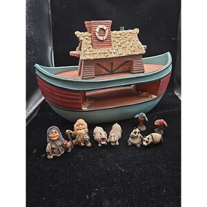 May include: A decorative boat-shaped figurine with a red and blue hull, topped with a thatched roof structure. Includes several small figurines of animals and people, including pandas and a seated figure.