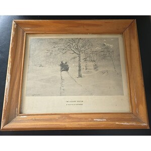 May include: Framed black and white print titled "The Country Doctor" by Paul Miller Hoffmaster. The artwork depicts a snowy winter scene with a horse-drawn carriage on a path. The frame is made of light brown wood.