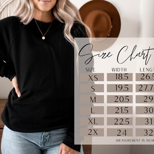 May include: A black sweatshirt with a size chart. The size chart shows measurements in inches for sizes XS to 2X. The sweatshirt is shown on a person wearing blue jeans.