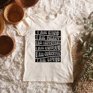 May include: A white t-shirt with a black graphic that reads "I am kind, I am smart, I am important, I am unique, I am creative, I am loved."
