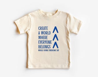 May include: A cream coloured t-shirt with blue text that reads "Create a world where everyone belongs" and "World Down Syndrome Day". Three blue upward pointing arrows are to the right of the text.