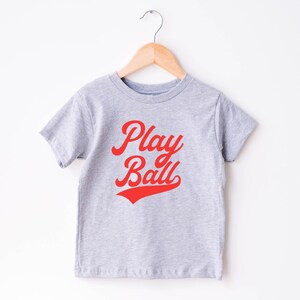 May include: Gray short-sleeved t-shirt with red text that says "Play Ball" in a retro font.
