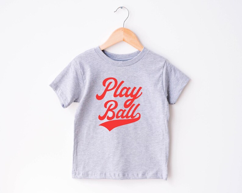 May include: Gray short-sleeved t-shirt with red text that says "Play Ball" in a retro font.