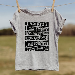 May include: A gray t-shirt with black text that reads "I am kind, I am smart, I am important, I am unique, I am creative, I am loved."