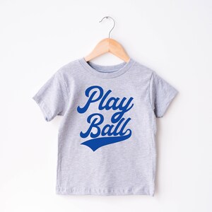 May include: A gray t-shirt with a blue graphic that says "Play Ball" in a retro font.