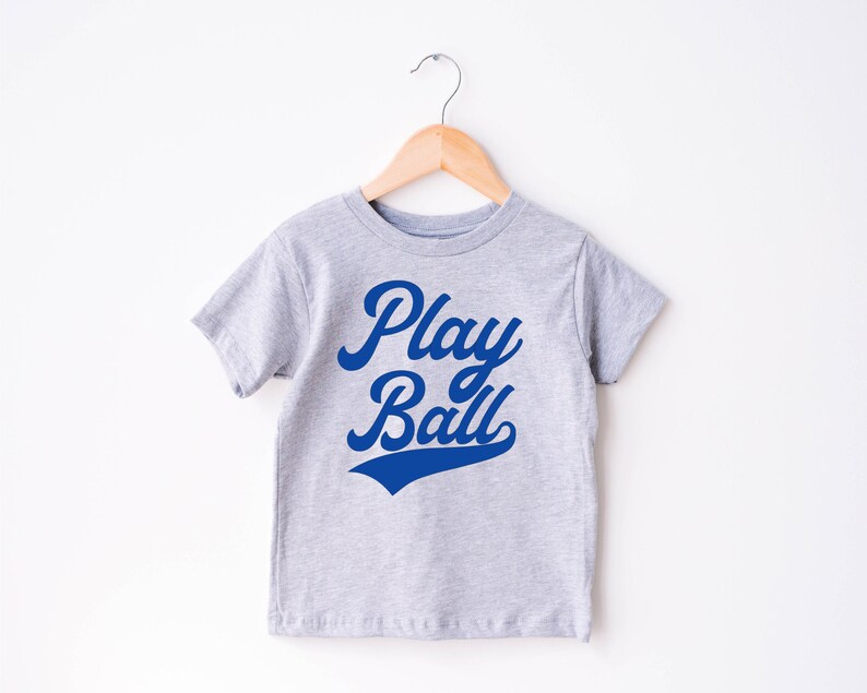 May include: A gray t-shirt with a blue graphic that says "Play Ball" in a retro font.