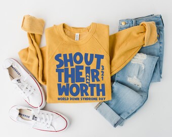 May include: Mustard yellow sweatshirt with the text "SHOUT THEIR WORTH" in blue, and "WORLD DOWN SYNDROME DAY". The sweatshirt is next to light blue jeans and white trainers with red trim.