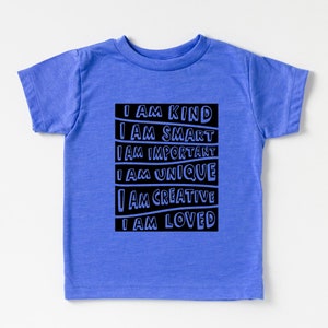 May include: A blue short-sleeved t-shirt with a black graphic that reads "I AM KIND, I AM SMART, I AM IMPORTANT, I AM UNIQUE, I AM CREATIVE, I AM LOVED".