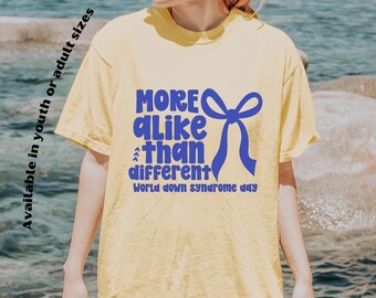 Könnte beinhalten: Hellgelbes T-Shirt mit blauem Text "MORE alike than different" und einer blauen Schleife. Der Text "World down syndrome day" ist ebenfalls enthalten. Erhältlich in Jugend- oder Erwachsenengrößen.