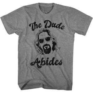 May include: A heather grey t-shirt with a black and white graphic of The Dude from The Big Lebowski. The text "The Dude Abides" is printed in black on the shirt.