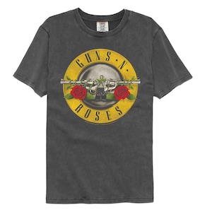 May include: Dark gray t-shirt featuring a distressed Guns N' Roses graphic. The design includes a skull, two revolvers, red roses, and the band's name in a yellow circle. The shirt has a crew neck and short sleeves.