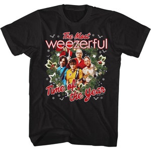 Può includere: Maglietta nera con un design natalizio con la band Weezer. Il design include una ghirlanda con accenti rossi e verdi, fiocchi di neve e il testo "The Most Weezerful Time of the Year".