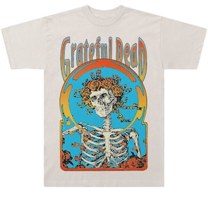 May include: A white t-shirt with a vintage-style graphic of a skeleton with a rose crown inside a blue circle. The text "Grateful Dead" is printed above the graphic.