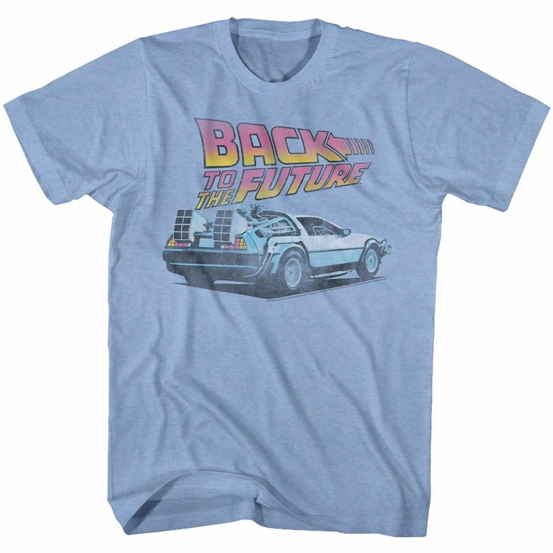 May include: A light blue t-shirt with a faded graphic of the DeLorean time machine from the movie "Back to the Future". The text "Back to the Future" is printed in pink, orange, and yellow.