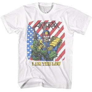 Puede incluir: Camiseta blanca con un gráfico desgastado de un personaje con casco y sosteniendo un arma. El gráfico está sobre un fondo de bandera estadounidense roja, blanca y azul. El texto "Anthrax" y "I am the law" están impresos en la camiseta.