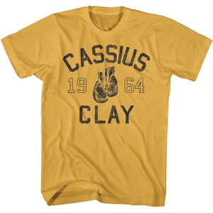May include: A yellow t-shirt with a black graphic print that says "CASSIUS 19 64 CLAY". The graphic includes a pair of boxing gloves.