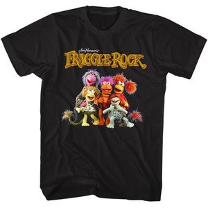 May include: Black t-shirt featuring the text "Jim Henson's Fraggle Rock" in gold lettering above a group of colorful Fraggle Rock characters. The characters include a variety of colors, including pink, orange, and green.