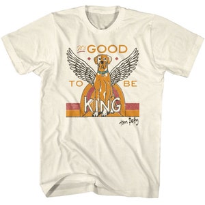 Pode incluir: Uma camiseta branca com um gráfico de estilo vintage de um cão com asas. O gráfico diz "It's Good To Be King" com "Tom Petty" escrito abaixo.