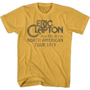 May include: A yellow t-shirt with a vintage-style graphic of Eric Clapton and his band. The text reads "Eric Clapton and His Band North American Tour 1979".
