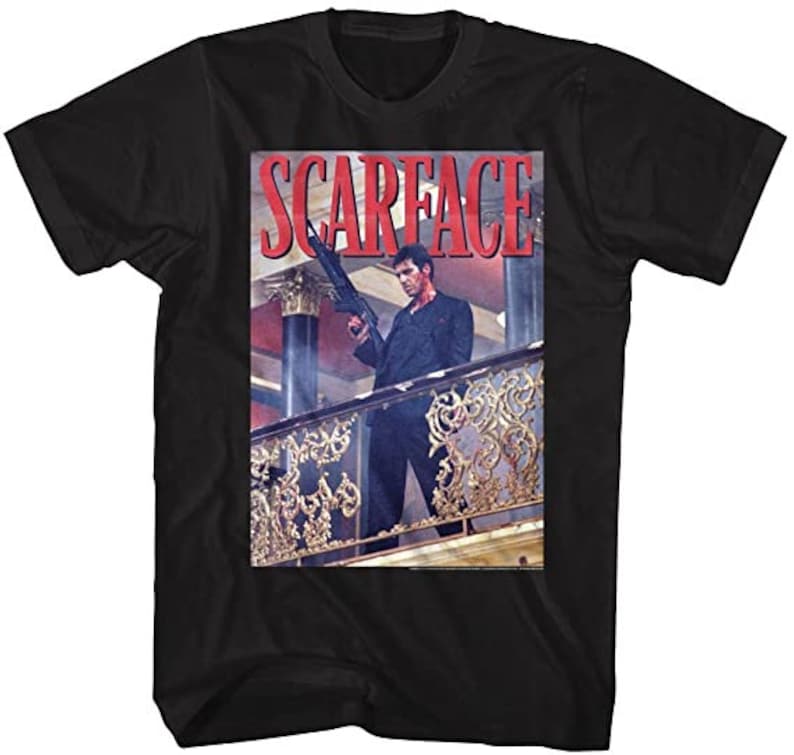 May include: Black t-shirt with a graphic print of a man holding a gun, standing on a balcony. The text "Scarface" is printed in red letters above the image.