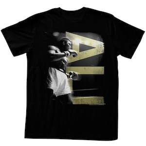 Könnte beinhalten: Schwarzes T-Shirt mit einem Grafikdruck eines Boxers im Ring mit dem Wort "ALI" in goldenen Buchstaben.