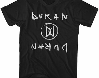 Puede incluir: Camiseta negra con un gráfico blanco del logotipo de la banda Duran Duran. El logotipo es un círculo con las letras "D" y "D" dentro, y el nombre de la banda está escrito arriba y abajo del logotipo.