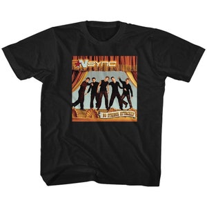 Op de afbeelding: Zwart T-shirt met een foto van de boyband *NSYNC op de voorkant. De foto toont de bandleden voor een rood en gouden gordijn met de woorden "No Strings Attached" op een banner eronder.