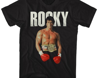 May include: Black t-shirt with a white "ROCKY" graphic and a picture of Sylvester Stallone as Rocky Balboa wearing boxing gloves and a championship belt.