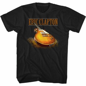 Op de afbeelding: Zwart T-shirt met een bruine en oranje elektrische gitaar en de tekst "ERIC CLAPTON" in oranje.