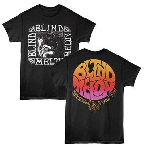 Puede incluir: Dos camisetas negras. Una presenta un gráfico blanco de una cara y las palabras "Blind Melon" en un cuadrado. La otra camiseta tiene un diseño circular con las palabras "Blind Melon" en naranja y rosa, con "Crammed in a Van Tour 1994" debajo.