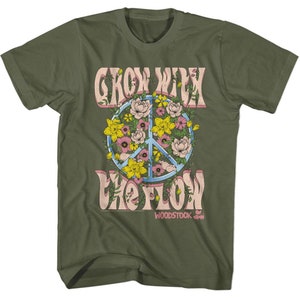 Op de afbeelding: Een groen T-shirt met een vredesteken omringd door bloemen en de tekst "Grow With The Flow" en "Woodstock" in roze letters.