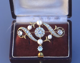 Puede incluir: Broche dorado vintage con diseño floral, engastado con piedras preciosas transparentes y perlas. El broche se exhibe en una caja forrada de terciopelo granate. El diseño presenta un grupo central de piedras y líneas curvas.