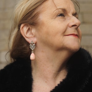 Peut inclure: Une paire de boucles d'oreilles pendantes avec une goutte de pierre rose et un sertissage argenté avec des strass transparents.