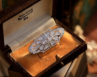 May include: A silver brooch with a geometric design and clear stones set in a vintage style. The brooch is in a brown velvet box with the inscription "Laura Pardalis San Lorenzo 43 Alioq".