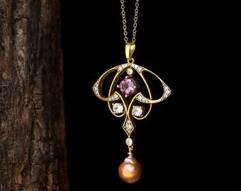 Peut inclure: Un collier pendentif en or avec une pierre rose centrale, entourée de pierres claires. Le pendentif présente un design Art nouveau avec une perle en forme de goutte. Le collier est sur fond noir.
