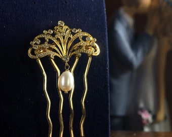 Puede incluir: Un peine de pelo dorado con una perla y adornos de cristal. El peine tiene cuatro púas.