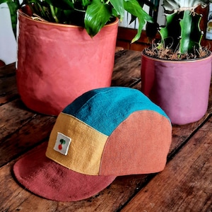 Peut inclure: Une casquette de baseball en tissu multicolore avec une cerise rouge brodée sur le devant. La casquette est faite d'un patchwork de tissu turquoise, jaune et orange.