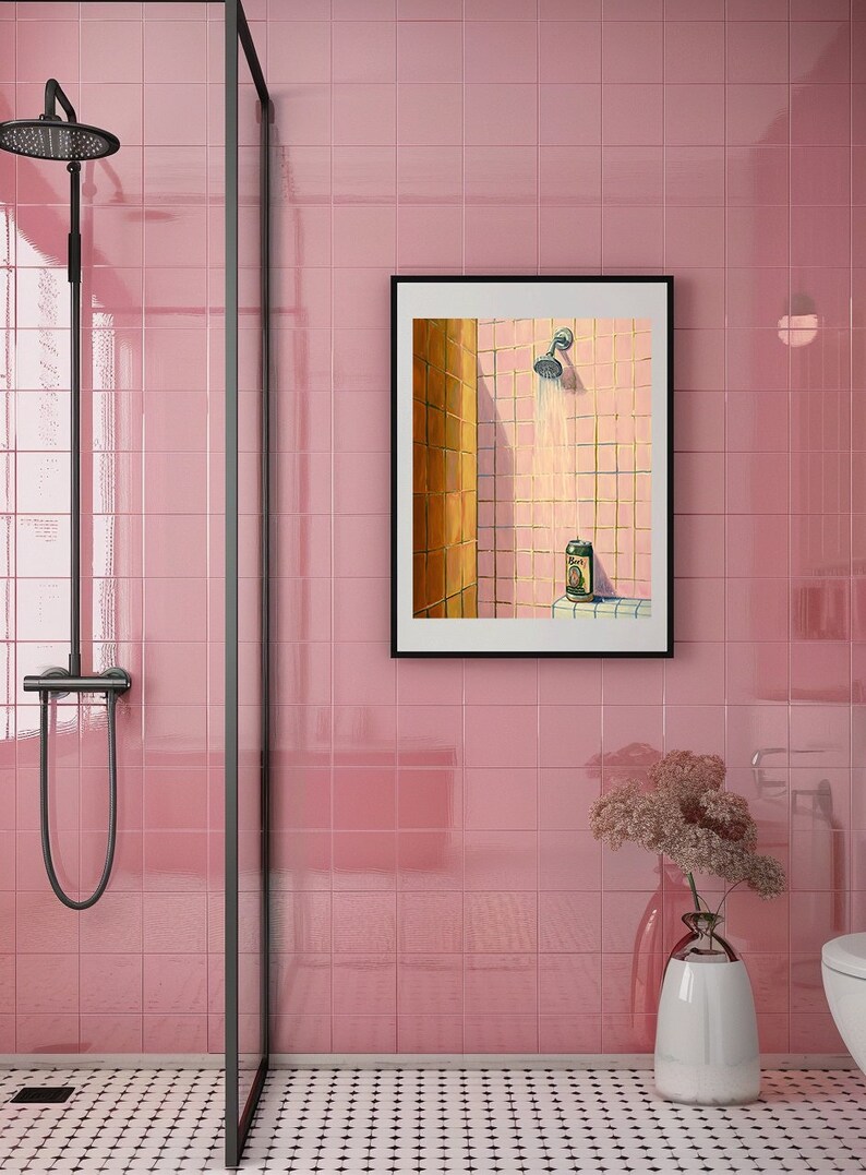 May include: A pink tiled bathroom with a black framed art print. The art depicts a shower scene with a beer can. A black shower fixture is visible, along with a glass shower door and a vase of flowers.