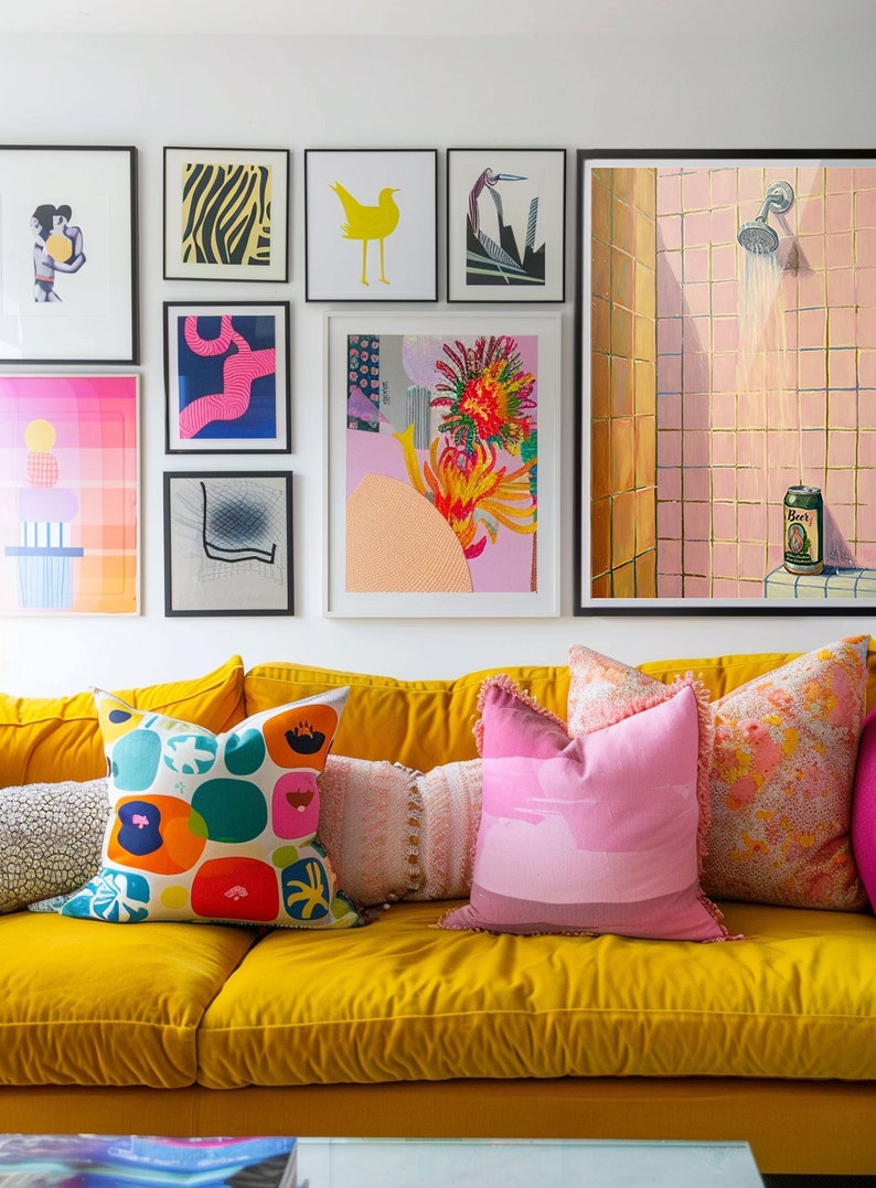 May include: A vibrant living room scene featuring a yellow velvet sofa adorned with colorful throw pillows. Artwork in black frames hangs on the white wall above. The art includes abstract prints and a painting of a shower.