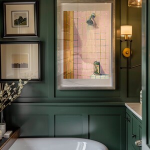 May include: A bathroom scene with a large white bathtub and a framed artwork depicting a shower with a beer can. The walls are dark green, and there are two framed pictures above the tub. A wall sconce provides additional lighting.