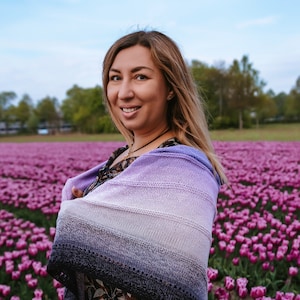 Peut inclure: Une femme portant un châle dégradé violet et bleu se tient dans un champ de tulipes violettes. Elle sourit et regarde la caméra.