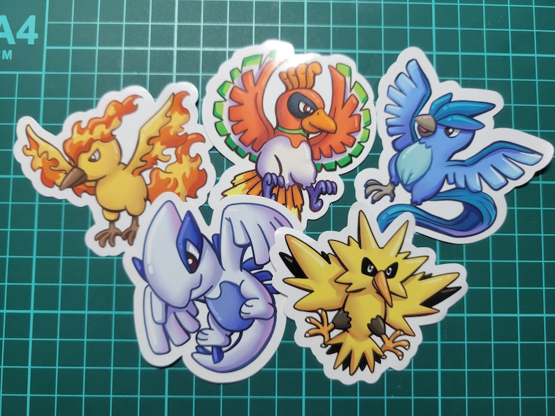 May include: Five colorful cartoon Pokemon stickers featuring the characters: Moltres, Articuno, Zapdos, Flareon, and Jolteon. The stickers are on a green grid background.