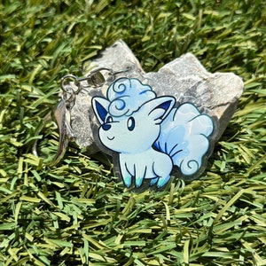 May include: A blue and white anime character keychain with a silver chain. The character is a fluffy, cloud-like creature with a curled tail.