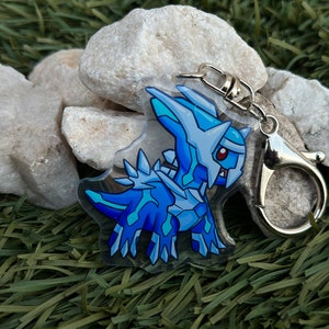 May include: A blue and white cartoon creature keychain with a silver metal key ring. The creature has a sharp, pointed head and a spiky back.