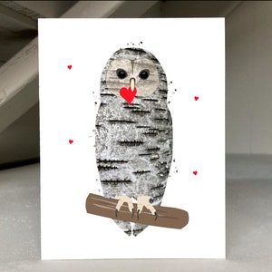 May include: A greeting card featuring a whimsical owl illustration. The owl has a textured, birch-like pattern in shades of gray and white, with a red heart-shaped beak. It is perched on a brown branch, with small red hearts scattered around.