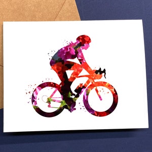 May include: Watercolor illustration of a cyclist on a road bike. The cyclist and bike are rendered in shades of red, pink, and purple, with a white background. The image is on a white card with a brown envelope.
